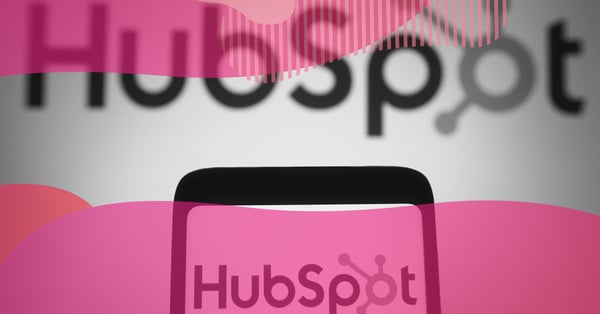 HubSpot logo displayed on a smartphone screen in focus, with the brand name blurred in the background and a pink overlay, representing the CRM platform for Hubspot clients.