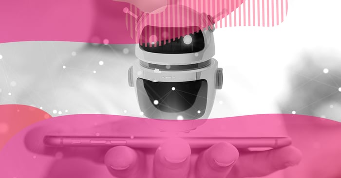 Ilustração em preto e branco de um mini robô flutuando acima de um smartphone na mão de uma pessoa, com elementos em rosa, representando um chatbot de inteligência artificial em dispositivos móveis.
