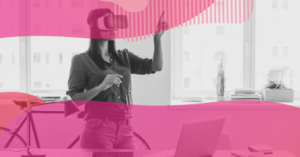 Mulher usando óculos de realidade virtual em um escritório, interagindo com o ambiente enquanto um notebook está sobre a mesa.