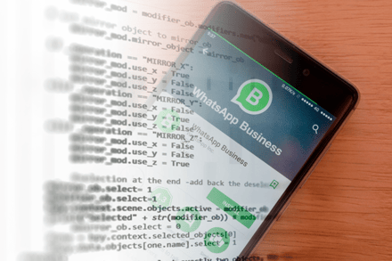 Smartphone displaying the WhatsApp Business installation screen, on a wooden table, with programming code superimposed, representing the technological integration of the tool with automations.