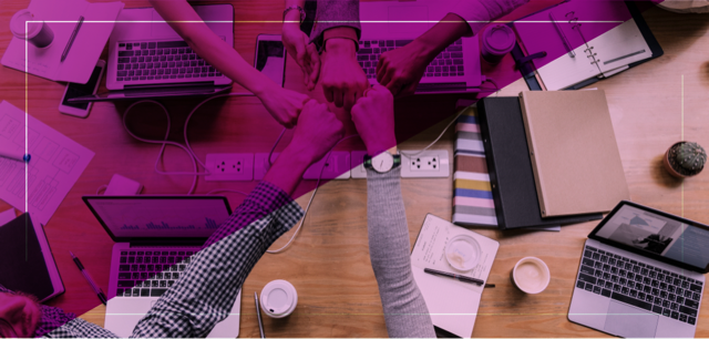Team gathered around a table with laptops and papers, making a collective gesture of unity with their fists, symbolizing collaborative work in managing image crises on social media.