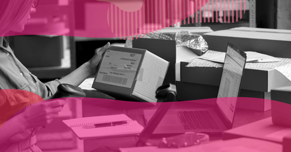 Person checking a shipping label and scanning a parcel at a desk with boxes and a laptop, representing e-commerce order fulfillment.