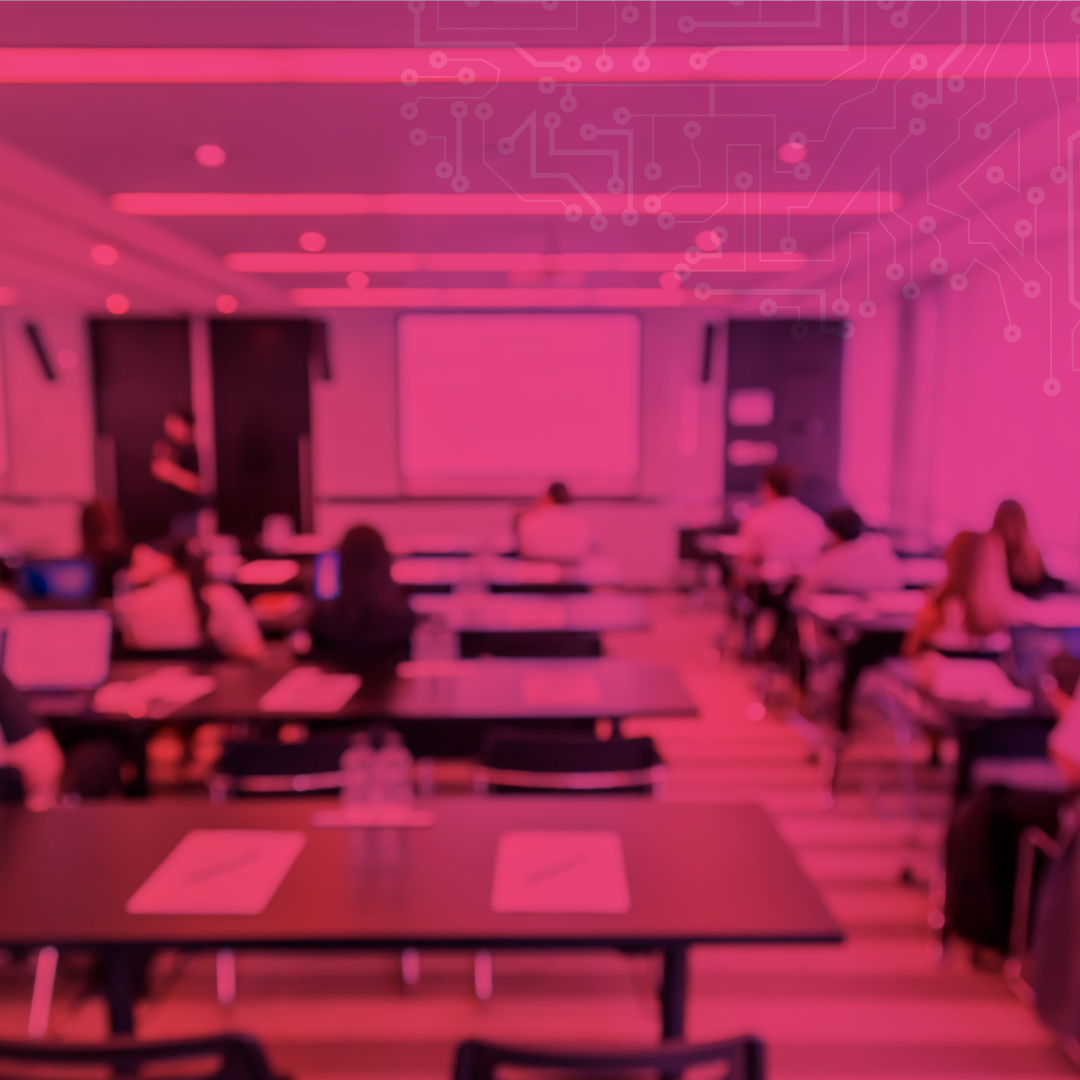Sala de aula com estudantes sentados em mesas, assistindo a uma apresentação no projetor, representando o ambiente acadêmico e o desafio da permanência estudantil.