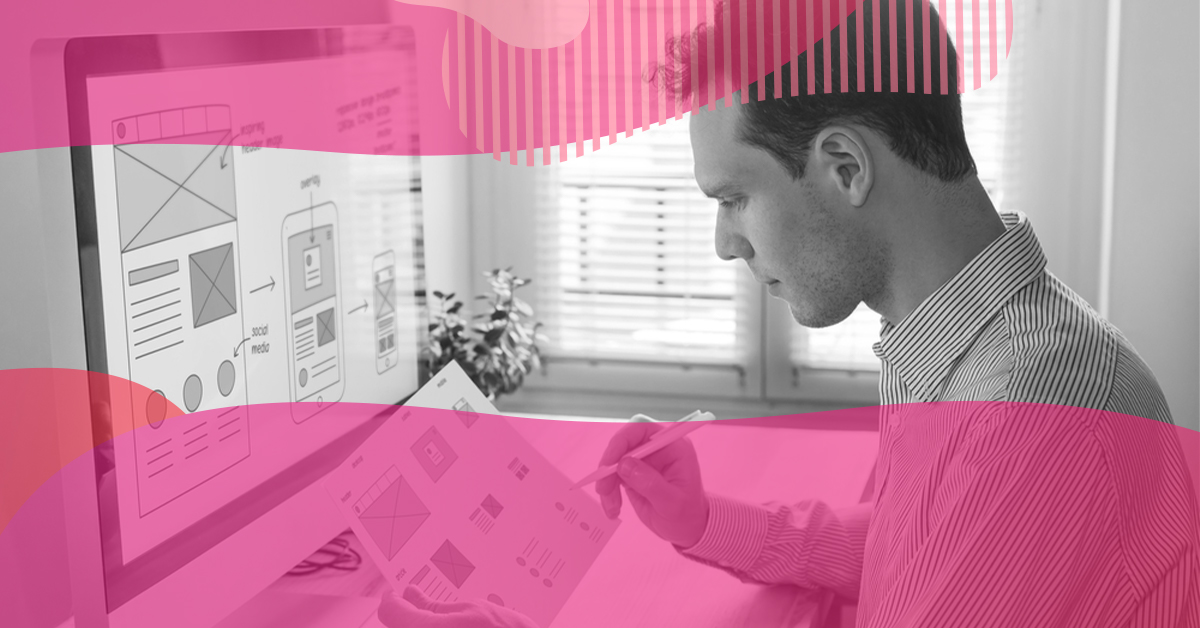 Designer reviewing on a computer the layout of a responsive website for desktop and mobile while holding printed wireframes.