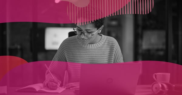 Pessoa usando óculos escreve em um caderno ao lado de um notebook, representando o trabalho de UX writing para melhorar a experiência do usuário em produtos digitais.