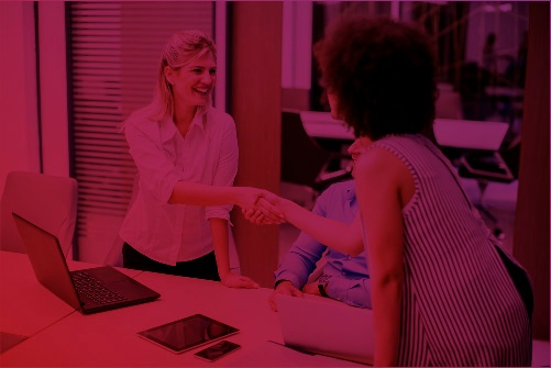 Two women shaking hands in a corporate environment, symbolizing partnership and acceptance in a context of student recovery in higher education.