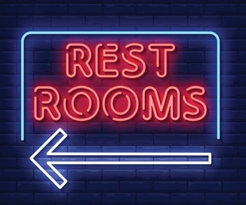 Neon sign with the words “REST ROOMS” and an arrow pointing left, illustrating how clear signage makes the user experience easier, just like UX writing in digital interfaces.